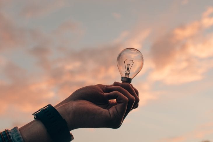 Person hält Glühbirne vor Himmel in der Hand als Zeichen von Kreativität. Beitragbild zum Thema: Kreativitätstechniken