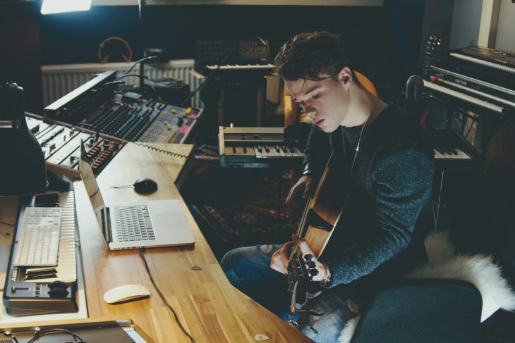 Mann spielt Gitarre in Aufnahmestudio beim Songwriting. Beitragsbild zum Thema: 4 chord songs