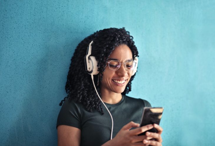 Junge Frau streamt Musik über ihr Handy zum Beitrag Musik Streaming Dienste im Vergleich