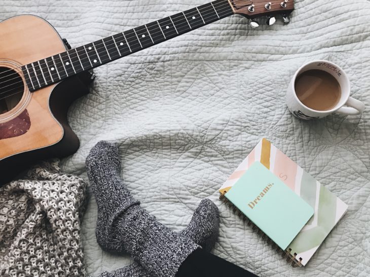 Effektiv üben - Jemand sitzt mit Gitarre, Notizbuch und Kaffee auf einer Decke