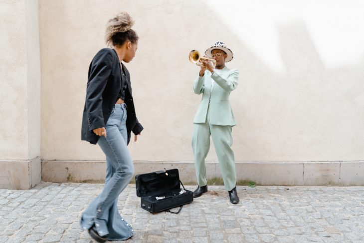 Eine Frau unterstützt einen Musiker, indem sie dem Posaunisten im blauen Anzug auf der Straße Geld in den Instrumentenkoffer wirft
