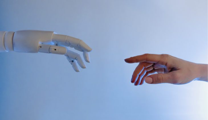 Hand von KI und menschliche Hand zeigen mit Ziegefingern aufeinander.