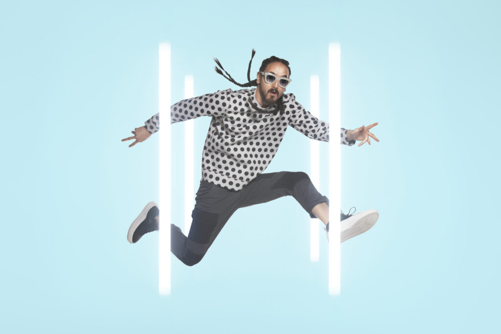 Steve Aoki posiert für ein Fotoshooting und springt zwischen Neonröhren in die Luft